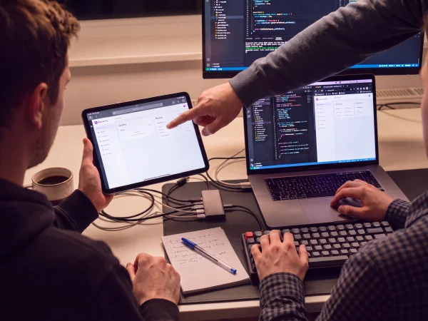 Developers reviewing an ordering interface on a tablet alongside application code on a laptop and monitor.